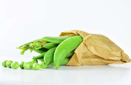 Green peas in kraft paper bag and others scattered, on white backgroundの写真素材