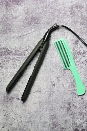 Hair straightener with isolated ceramic plates together with a long comb, on a stone background....