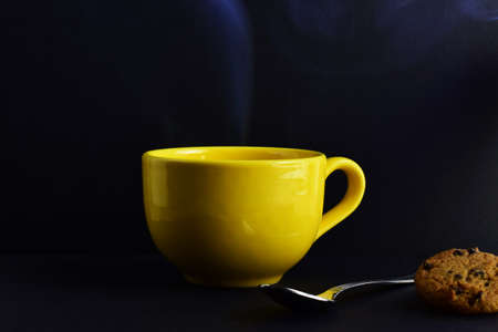 Yellow, hot mug, rising smoke, black background and copy space.の写真素材