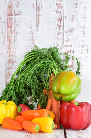 Assorted peppers and bunch of carrots on light colored rustic wood. Copy space.