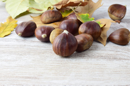 Close up. Chestnuts on the table and scattered natural leaves. Copy space.