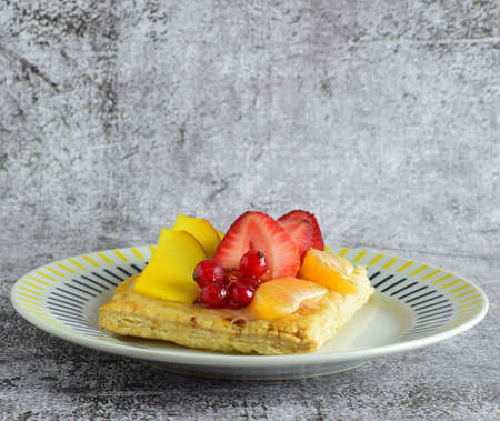 Fruit tartlet, red currants, mango, tangerine, presented on porcelain plate. Stone background and copy space.の写真素材