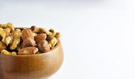 Assortment of dried fruits, hazelnuts, walnuts and almonds in a wooden bowl, light background.
