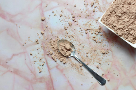 Zenith view, spoon with chocolate powder, next to small porcelain bowl on marble with abstract...