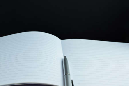 Silver ballpoint pen on notebook, black background.の写真素材