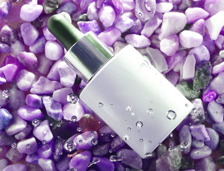 Dropper, cosmetic under wet surface and with water drops, on small purple stones.の写真素材