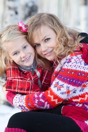 Mother and her daughter are sitting close each other in park in winter. They are happy and are smiling.の写真素材