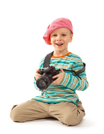 Cheerful little boy is a photographer  He holds the camera  He wears a beret, red scarf, striped sweater and beige pants  の写真素材