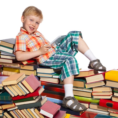 Little boy on a pile of books holds a tablet computer in his hands.の写真素材