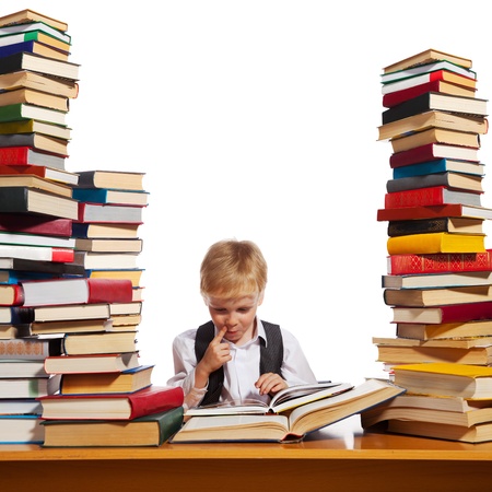 Little boy is reading interesting book. High stacks of books are on the table near him.の写真素材
