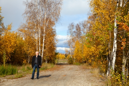 Elderly man with gray beard for a walk in the forest at the beginning autumnの写真素材