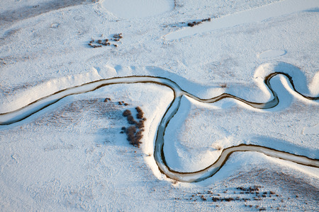 Aerial view over snowy fields with creek which fancifully winds between snowdrift の写真素材