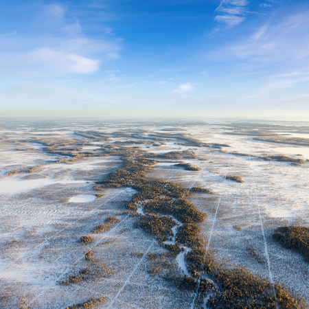 The Aerial view the river on snow-covered forest plain in time of cloudy winter evening. Crowns of coniferous trees are lighted up by a bright setting sun.の写真素材