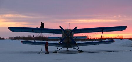Filling of airplane fuel before takeoff on the rural airfield during winter sunrise.の写真素材