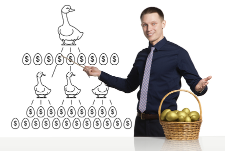 Young businessman showing scheme of successful business. In front of him is basket with golden eggs on the table. Ducks which lay golden eggs on the scheme.の写真素材