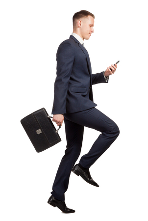 side view of jumping businessman with his briefcase, watching on the mobile phone on white backgroundの写真素材