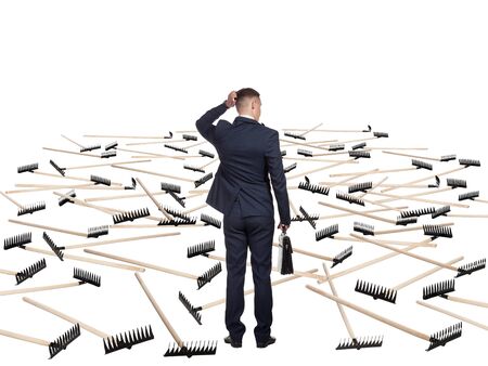 Young businessman in a suit and with a briefcase is undecided before the field that hosts a lot of rakes. He is afraid to move further. Concept of difficulty of deciding.の写真素材