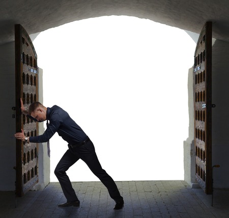 Young businessman opens heavy old gate to move on.の写真素材