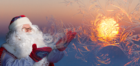 Santa Claus is blowing on window glass with frost and create amazing patterns, where the setting sun is reflected.の写真素材