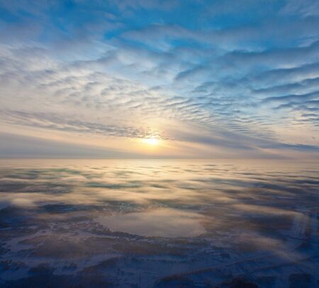 Aerial view of a cloudy sunset while flying above the clouds. Light layers of clouds look as waves.の写真素材