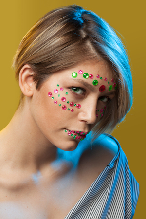 Young woman with red and green rhinestones on her face on yellow background.の写真素材