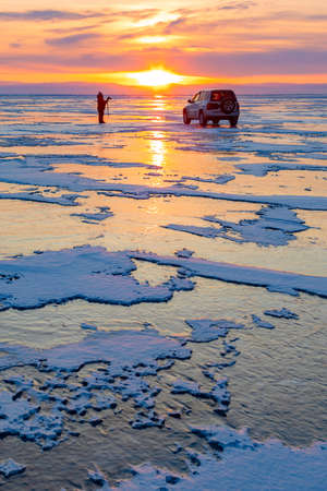 Beautiful sunset on Lake Baikal in winter. A lone tourist standing and admiring the fabulous landscape.の写真素材