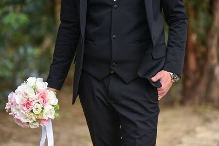 Groom and bouquet in hand close-up, dressing, man's style, stylish man. Elegant young handsome man. Men's jacket, hand cover the button. Business style.の写真素材