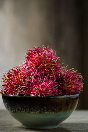 Red rambutan in ceramic bowl, still life image dark tone.の写真素材