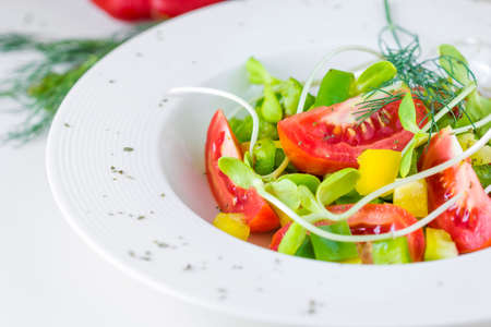 Fresh spring salad. tomatoes, yellow and green pepper,Sunflower sprouts in a bowl on a white backgroundの写真素材