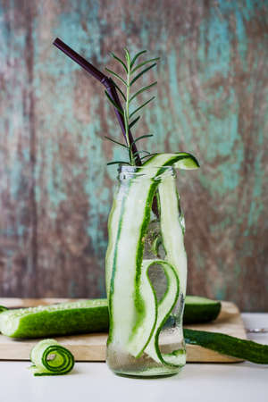 Glass bottle of cucumber and rosemary on wooden tableの写真素材