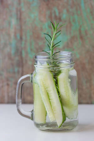 glass jar of cucumber and rosemary on wooden tableの写真素材