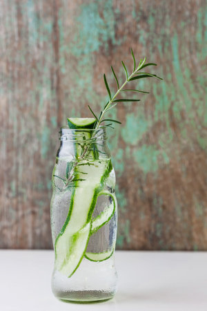 Glass bottle of cucumber and rosemary on wooden tableの写真素材