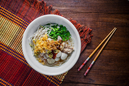 bowl of asian noodles with vegetables and pak on wooden table.