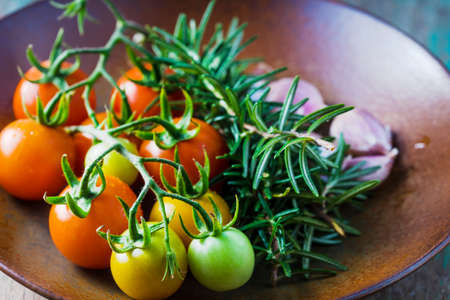 Cherry tomatoes, garlic and rosemary in ceramic plateの写真素材