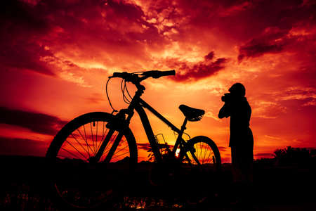 Silhouette of boy and bicycle on sunset backgroundの写真素材