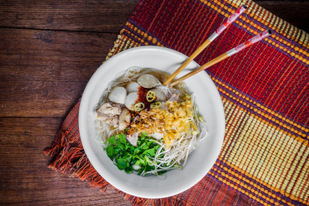 bowl of asian noodles with vegetables and pak on wooden table.