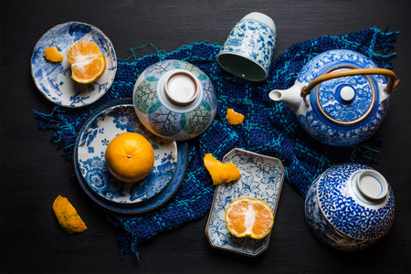 Whole and slice oranges fruits on ceramic plate over black wooden table. Top view.