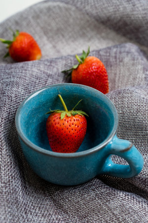 Fresh Strawberry in blue ceramic cup on gray dish clothの写真素材