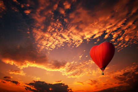 Red hot air balloon in the shape of a heart, Colorful hot-air balloon flying over sunsetの写真素材