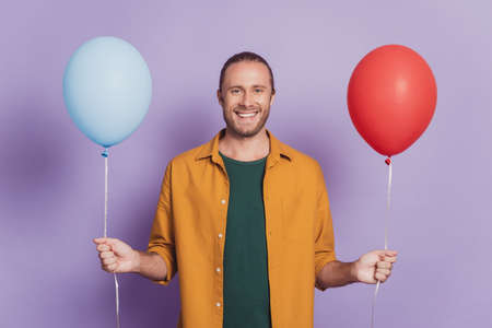 Close up portrait of positive man beaming smile hold two air balloons on purple wallの素材 [FY310167289886]