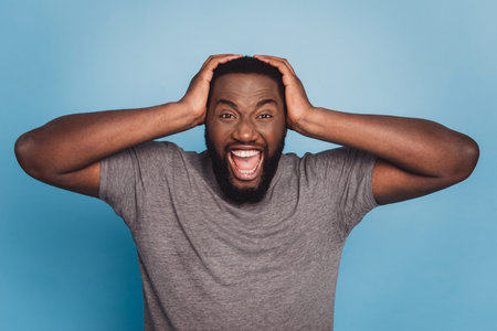 Angry irritated young african man screaming looking camera isolated on blue color background
