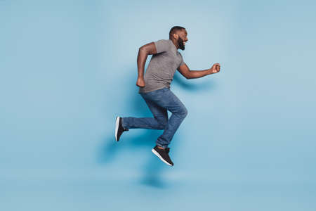 Full length view of afro guy jumping running isolated on blue backgroundの写真素材