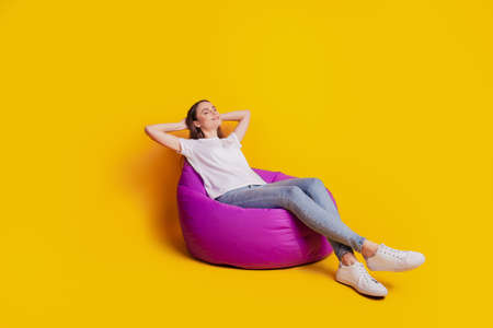 Profile photo of dreamy relaxing lady sit beanbag relax wear white t-shirt posing on yellow backgroundの写真素材