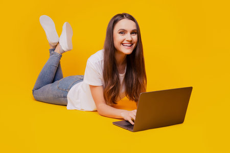 Photo of dreamy teen lady hold netbook work lay floor wear white t-shirt posing on yellow background
