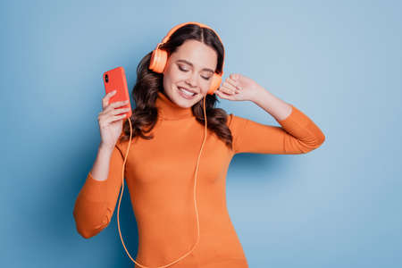 Pretty cool girl listening to music in headphones hold phone close eyes dance over blue backgroundの写真素材