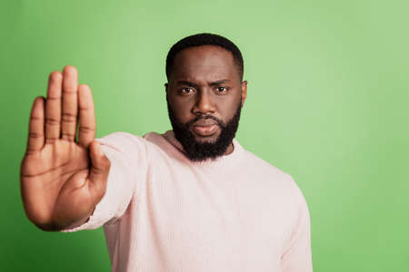 Photo of serious guy raise palm make stop signal wear white shirt over green backgroundの写真素材