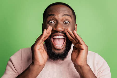 Photo of cheerful crazy excited guy open mouth hold palms scream message wear white shirt over green backgroundの写真素材