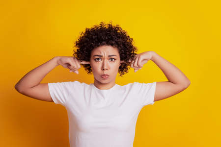 Picture of african student lady with fingers cover ears on yellow backgroundの写真素材