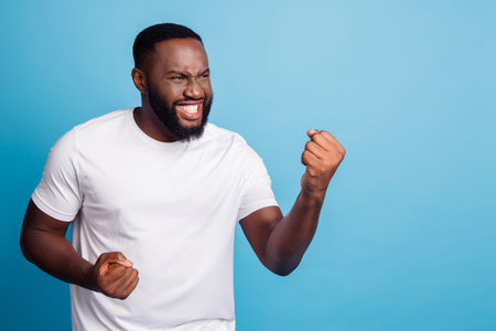 Portrait of positive crazy man raise fists celebrate win over blue background