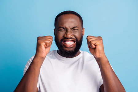 Photo of astonished crazy cheerful winner man raise fists close eyes beaming smile wear white...